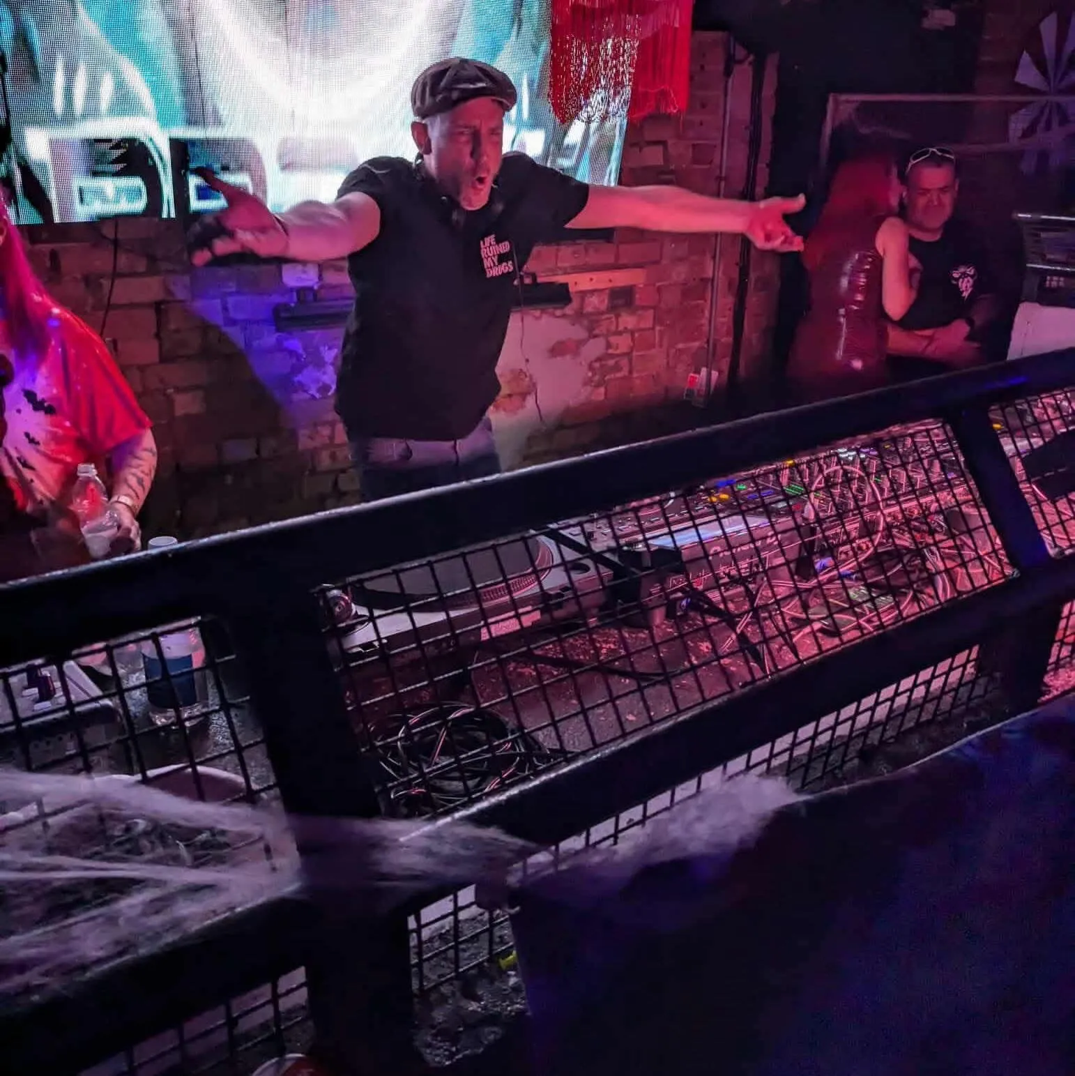 Carl Nicholson performing at a DJ booth under red and purple club lights